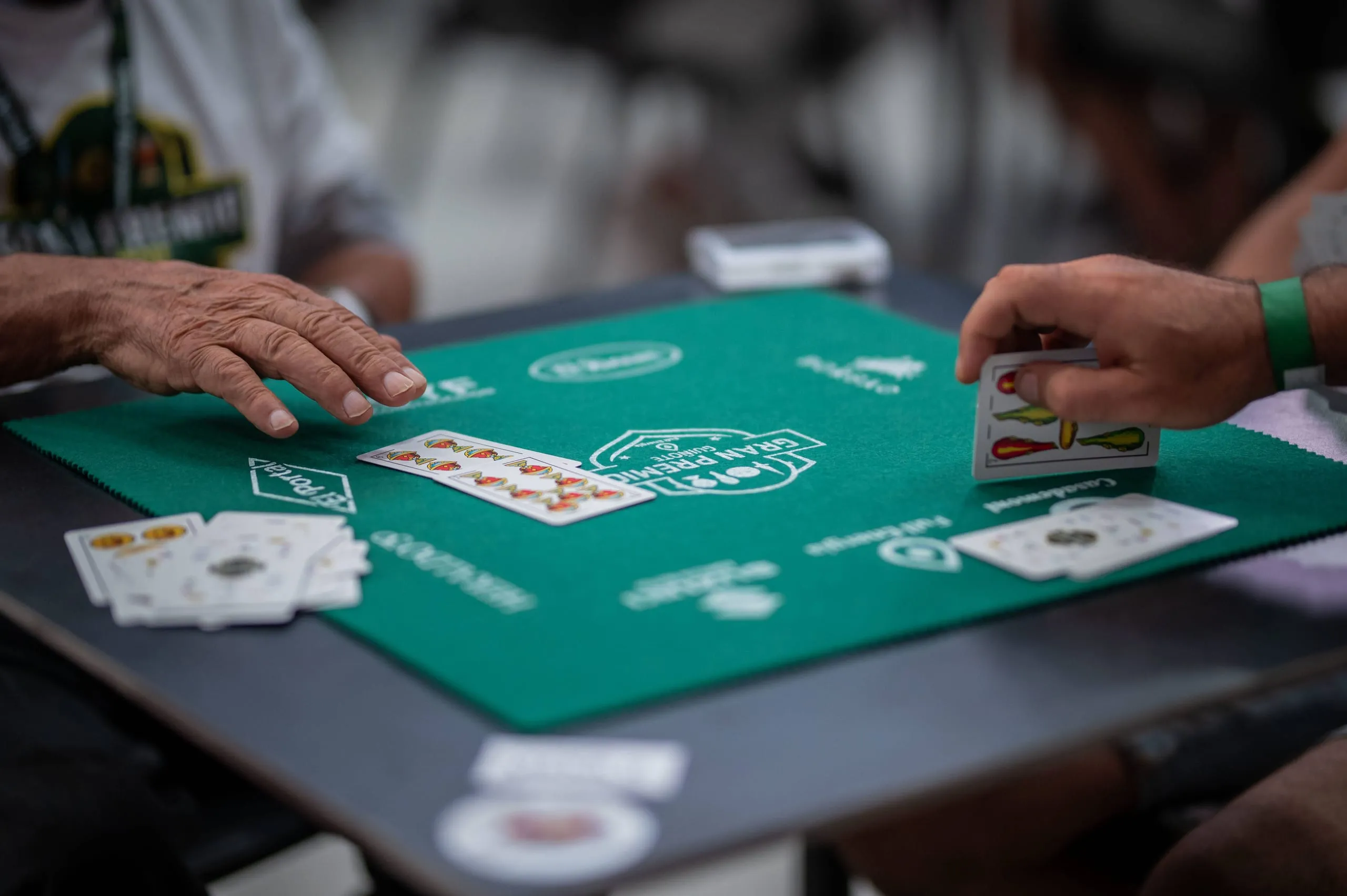 Primer plano de dos manos jugando una baza sobre el tapete verde del torneo.